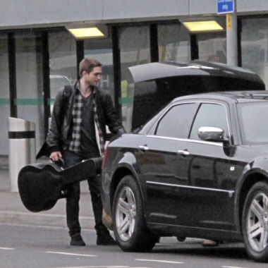 Robert Pattinson coi capelli corti e la chitarra in mano all'aeroporto di Londra